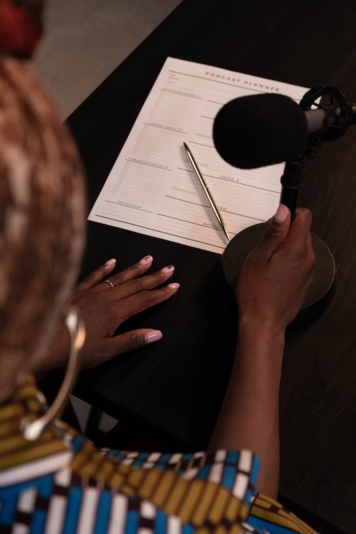 An overhead view of a person with a microphone and podcast planner on a desk.