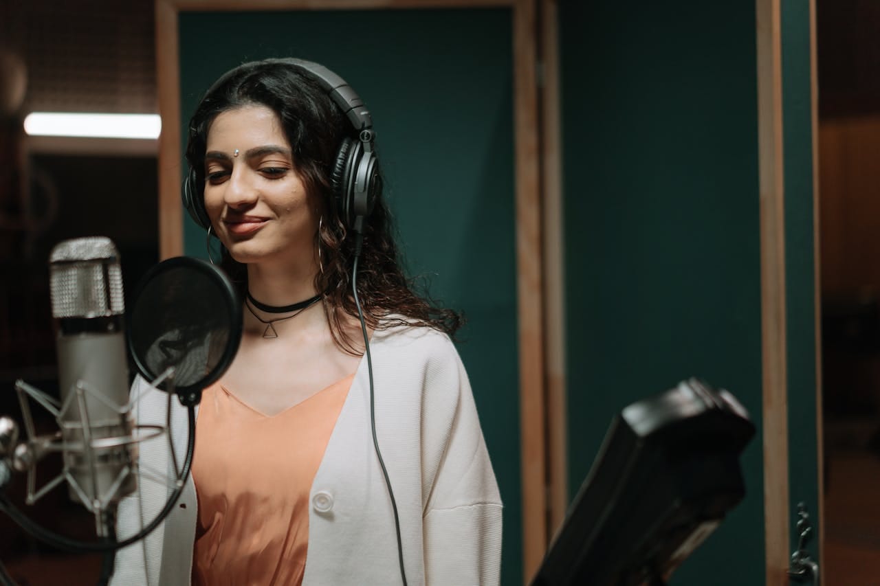 Woman singing into a microphone in a professional music studio wearing headphones.